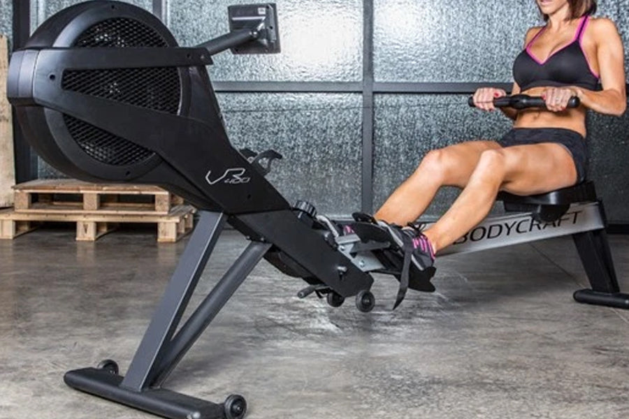 BodyCraft VR400 Pro black rowing machine with large fan wheel, used by woman in gym setting
