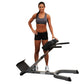 Woman wearing gray sports bra and black shorts posing with Body-Solid 45-degree hyperextension machine on white background