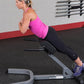 Woman in magenta tank top and black capris using 45-degree hyperextension machine in gym setting