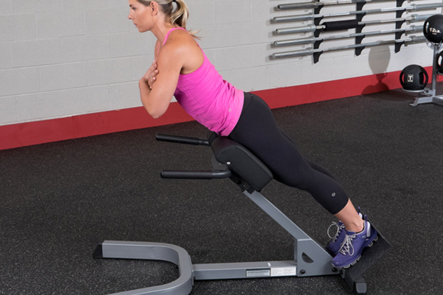 Woman in magenta tank top and black capris using 45-degree hyperextension machine in gym setting