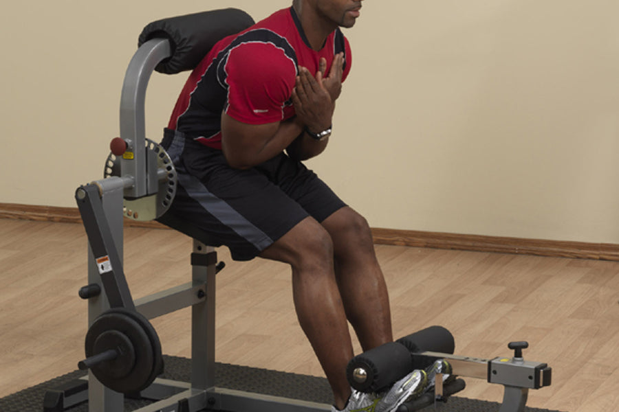 Man wearing red and black athletic shirt using gray and black stationary ab and back exercise machine with foot pedal