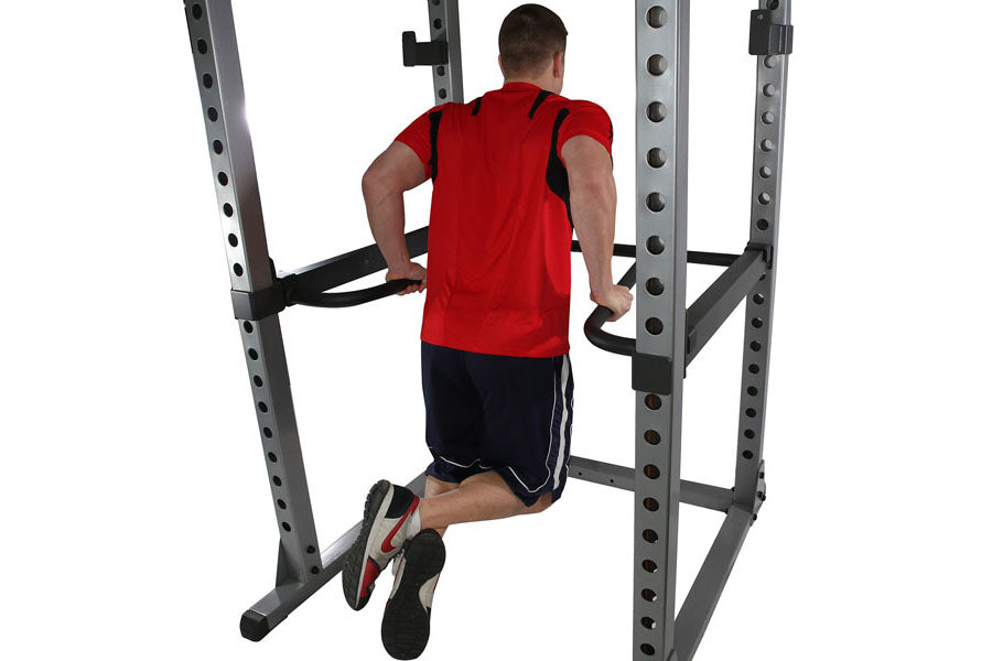 Man wearing red t-shirt and black shorts using dip bars on Body-Solid power rack with white background