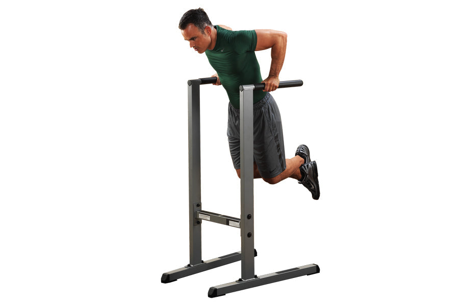 Man performing dip exercise on Body-Solid black steel dip station with horizontal bar, worn on white background
