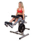 Woman in red sports bra and black shorts using gray and black leg extension machine with weighted plate, on white background