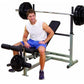 Male model wearing white sleeveless shirt and blue shorts seated on gray and black weight bench with barbell and leg extensio
