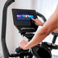 User interacting with Bowflex Max Trainer M9 elliptical machine with touchscreen display showing fitness app interface