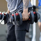 Person holding pair of black and red adjustable dumbbells with numbered weight dial, gym setting