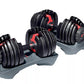 Pair of black adjustable dumbbells with red handles and weight selection dials on gray base, on white background