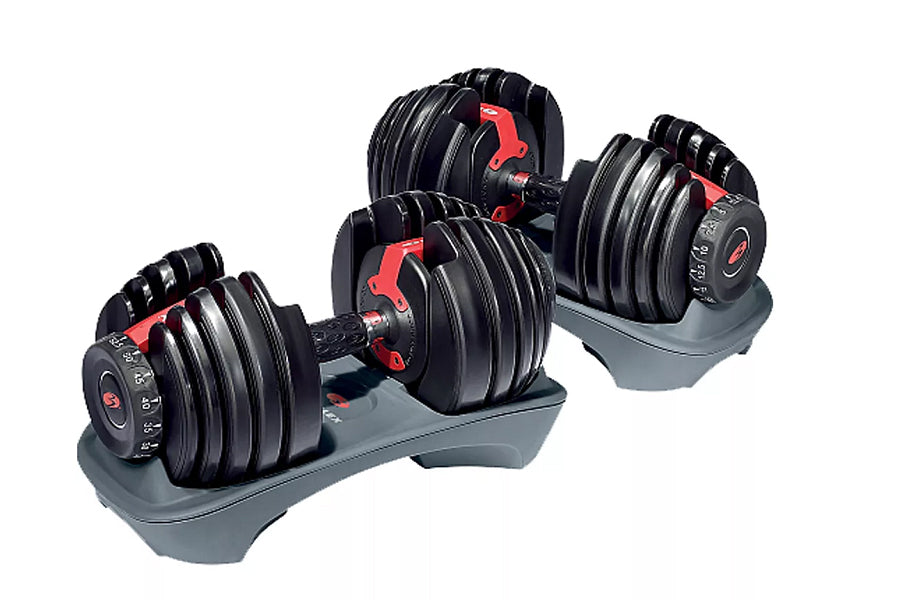 Pair of black adjustable dumbbells with red handles and weight selection dials on gray base, on white background