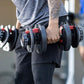 Man holding adjustable black and red Bowflex SelectTech dumbbells with numbered weight dial, worn in gym setting