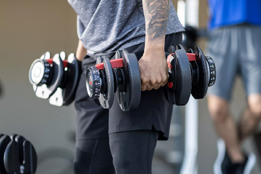 Man holding adjustable black and red Bowflex SelectTech dumbbells with numbered weight dial, worn in gym setting