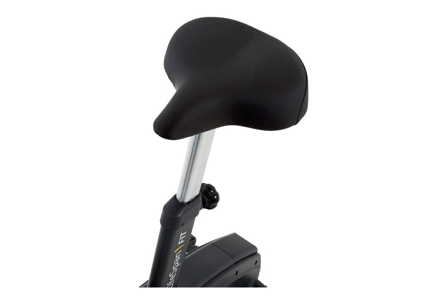 Black cushioned seat with silver metal post on upright exercise bike, isolated on white background