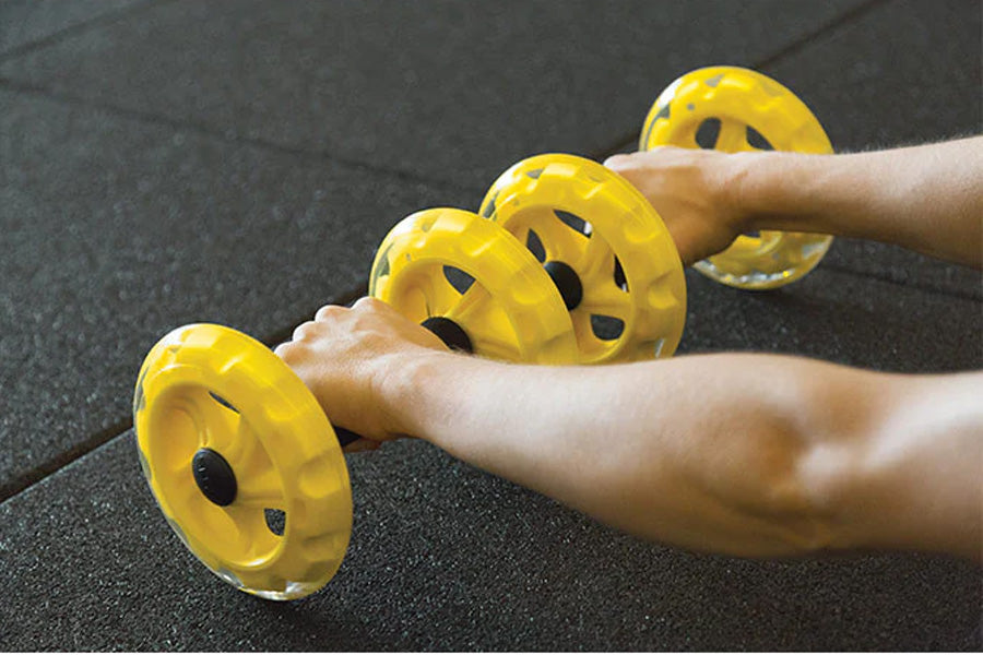 SKLZ COREwheels yellow core training wheels with ventilation holes held in hands on dark mat