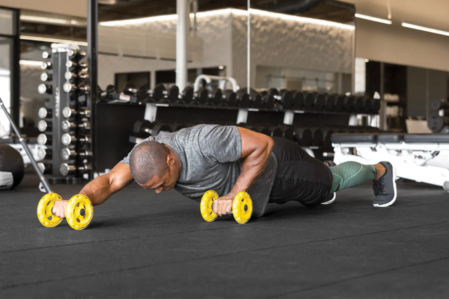 Man in plank position holding yellow dumbbells in modern gym setting