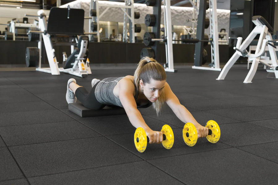 Woman performing plank exercise with yellow SKLZ COREwheels on black gym floor