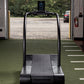 Black curved treadmill with digital display mounted on arch, shown on synthetic turf in fitness showroom
