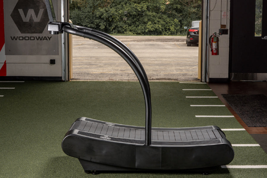 Black curved treadmill with arched running deck and dual handles, positioned in RV interior with open door view
