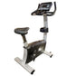 Upright exercise bike with black and gray frame, padded seat, handlebar console display, and silver base on white background