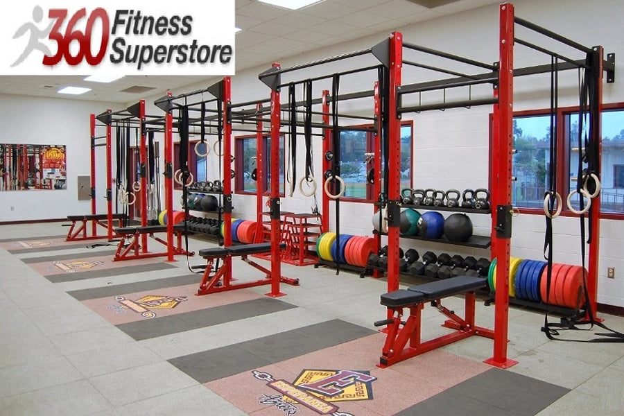 Red and black commercial gym rig system with pull-up bars, weight plates, kettlebells, and exercise balls in fitness facility