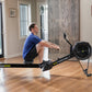 Man in blue shirt using black Concept2 RowErg rowing machine in modern home gym with wood flooring
