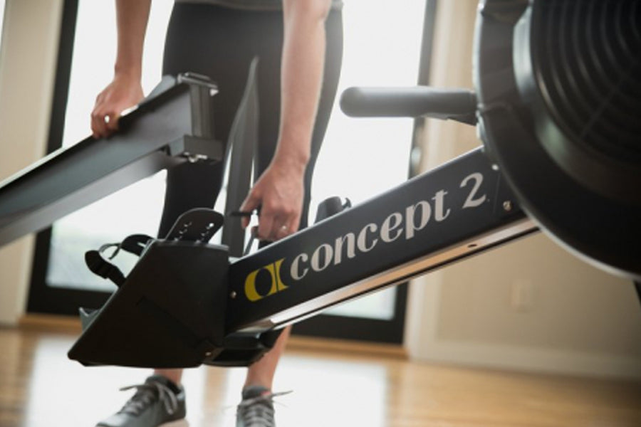 Concept2 RowErg indoor rowing machine with black frame and gold lettering, person using equipment with hands on handlebar