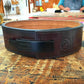 Dark brown leather belt with black metal buckle and embossed logo on workbench, cork lining visible on inner band