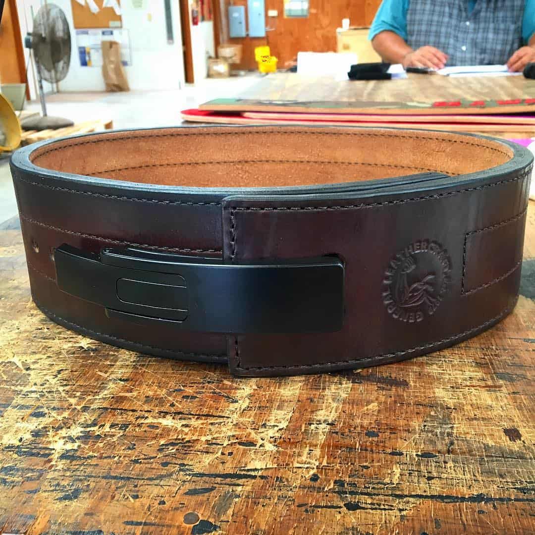 Dark brown leather belt with black metal buckle and embossed logo on workbench, cork lining visible on inner band