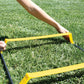 Person holding yellow and black agility ladder on green grass outdoors