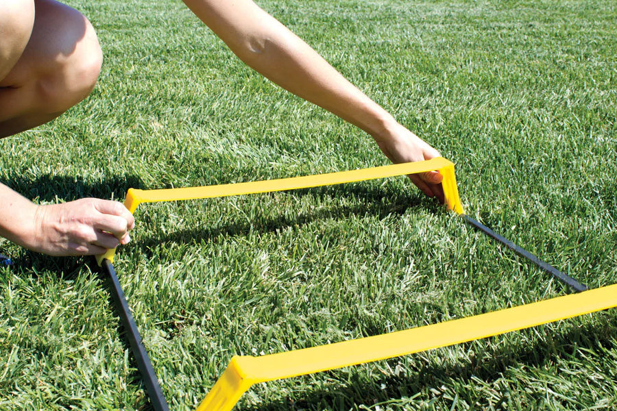 Person holding yellow and black agility ladder on green grass outdoors