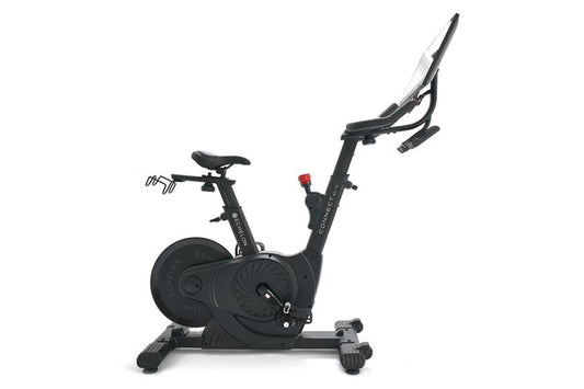 Black upright exercise bike with digital display, adjustable handlebars, padded seat, and weighted flywheel, on white backgro