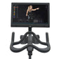 Black indoor exercise bike with digital console displaying workout metrics and video instruction from trainer on white backgr