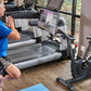 Man in blue shirt doing squat exercise on stationary bike with digital screen in home gym studio
