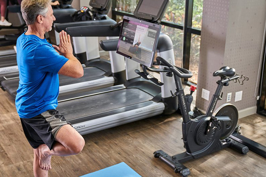 Man in blue shirt doing squat exercise on stationary bike with digital screen in home gym studio