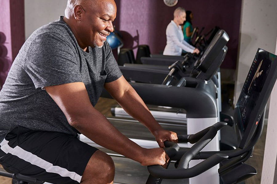 Man in gray t-shirt and black shorts using black Echelon Connect stationary bike with digital screen in gym setting