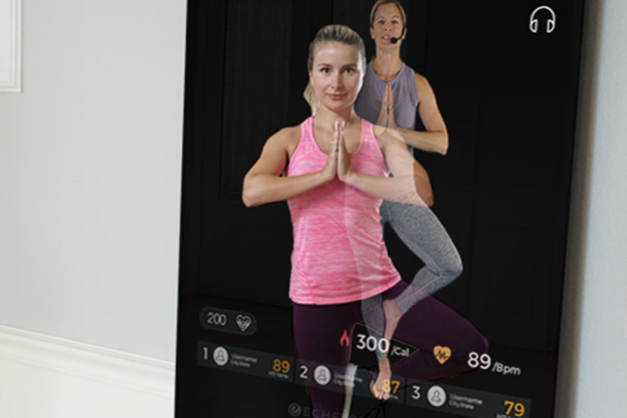 Echelon Reflect Touch 50 smart fitness mirror displaying woman in pink tank top and gray leggings performing yoga pose with i
