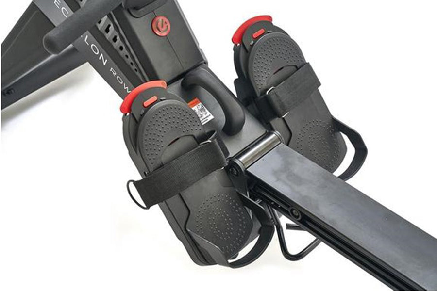 Echelon rowing machine footrests with black perforated material, red straps, and metal frame on white background
