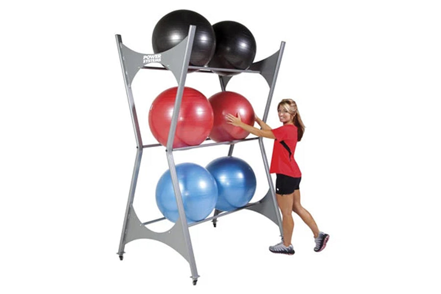 Gray metal storage rack holding six stability balls in black, red, and blue, with woman in red shirt demonstrating use