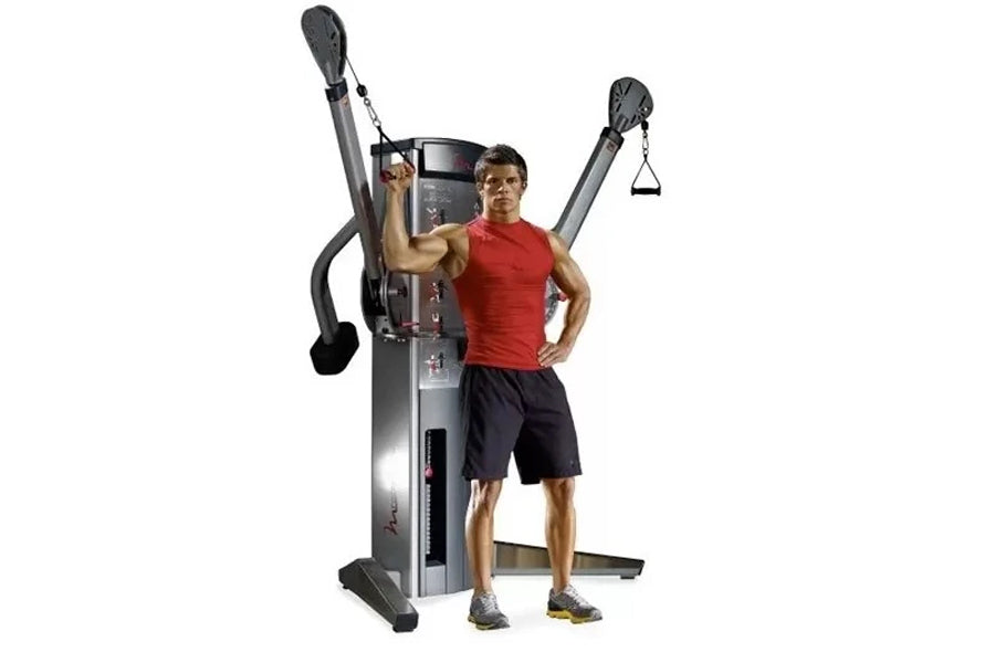 Man in red tank top and black shorts demonstrating dual cable cross machine with adjustable arms and weight stack on white ba
