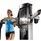 Woman in blue tank top and black shorts using dual cable crossover exercise machine with adjustable arms on white background