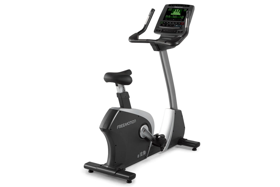 Black and gray upright exercise bike with digital display console showing green metrics, padded seat, and handlebars on white