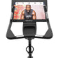 Black upright exercise bike with tablet display screen showing fitness content, gray handles, and pedal base on white backgro