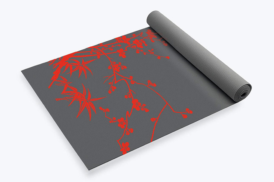 Gray yoga mat with red botanical branch design, partially rolled, on white background
