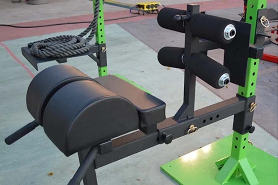 Warrior Glute-Ham Developer attachment with black padded seat and leg extension platform, mounted on green and black power ra