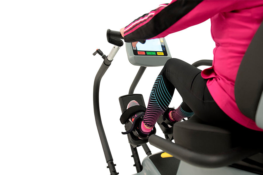 Person wearing hot pink jacket and black striped leggings using Physiostep LXT recumbent elliptical with digital display cons