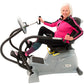 Woman wearing hot pink and black athletic jacket demonstrating gray Physiostep LXT recumbent elliptical cross trainer with bl