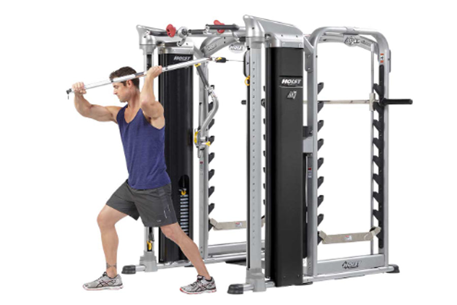 Man in blue tank top using Hoist Mi7Smith functional training system with cable machine, silver and black metal frame on whit