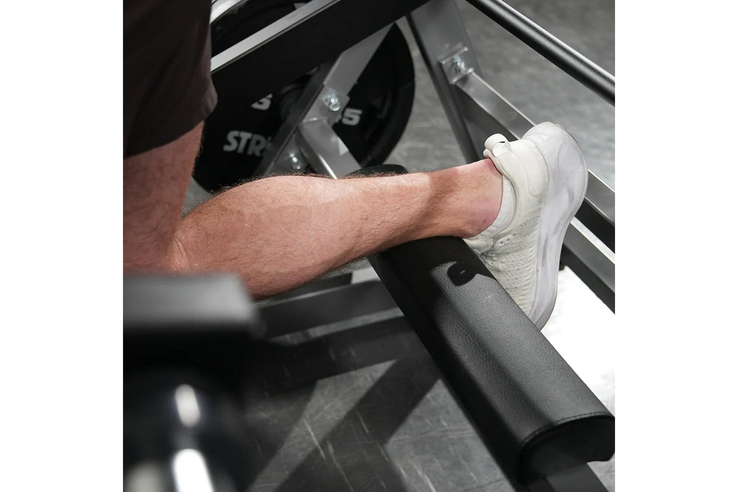 Man wearing white sneaker on Hammer Strength squat machine foot platform, demonstration of proper foot placement