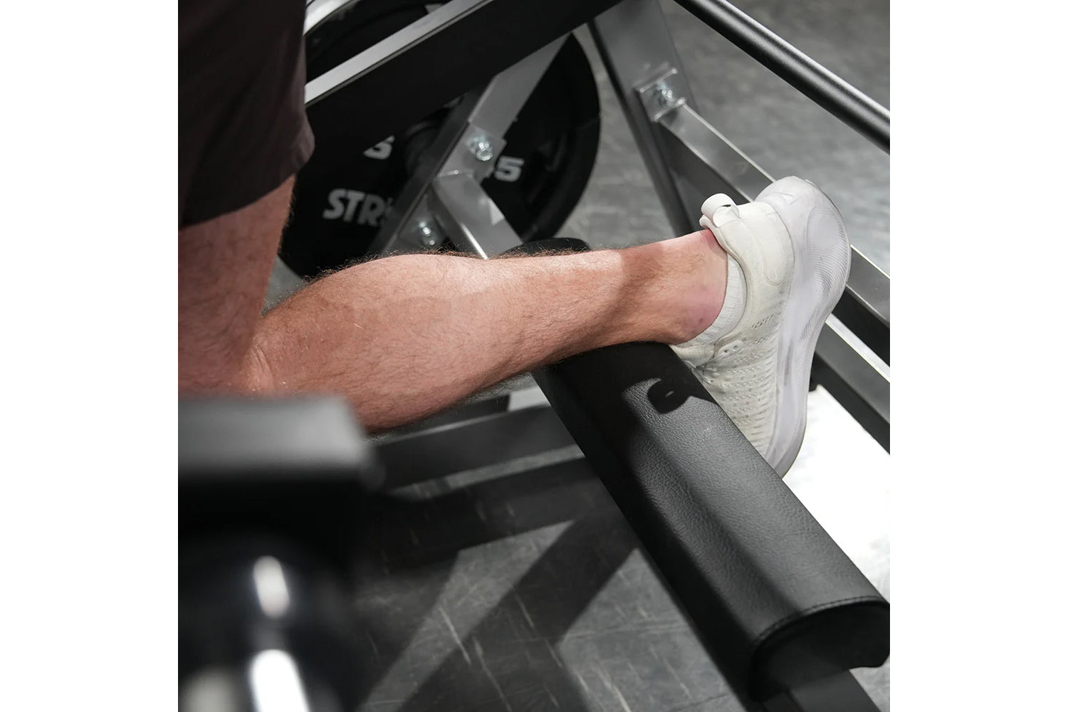 Man wearing white sneaker on Hammer Strength squat machine foot platform, demonstration of proper foot placement
