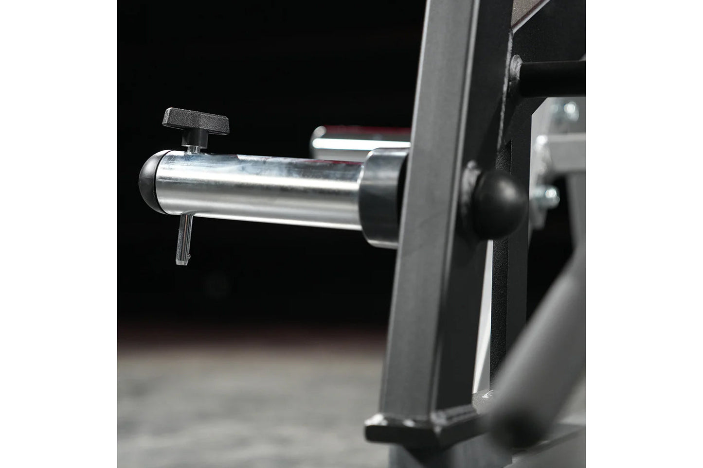 Hammer Strength ground base multi-squat machine with polished steel bar and black frame on black background, detail view
