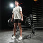 Man wearing light gray t-shirt and black shorts holding dumbbells in gym setting with Hammer Strength equipment